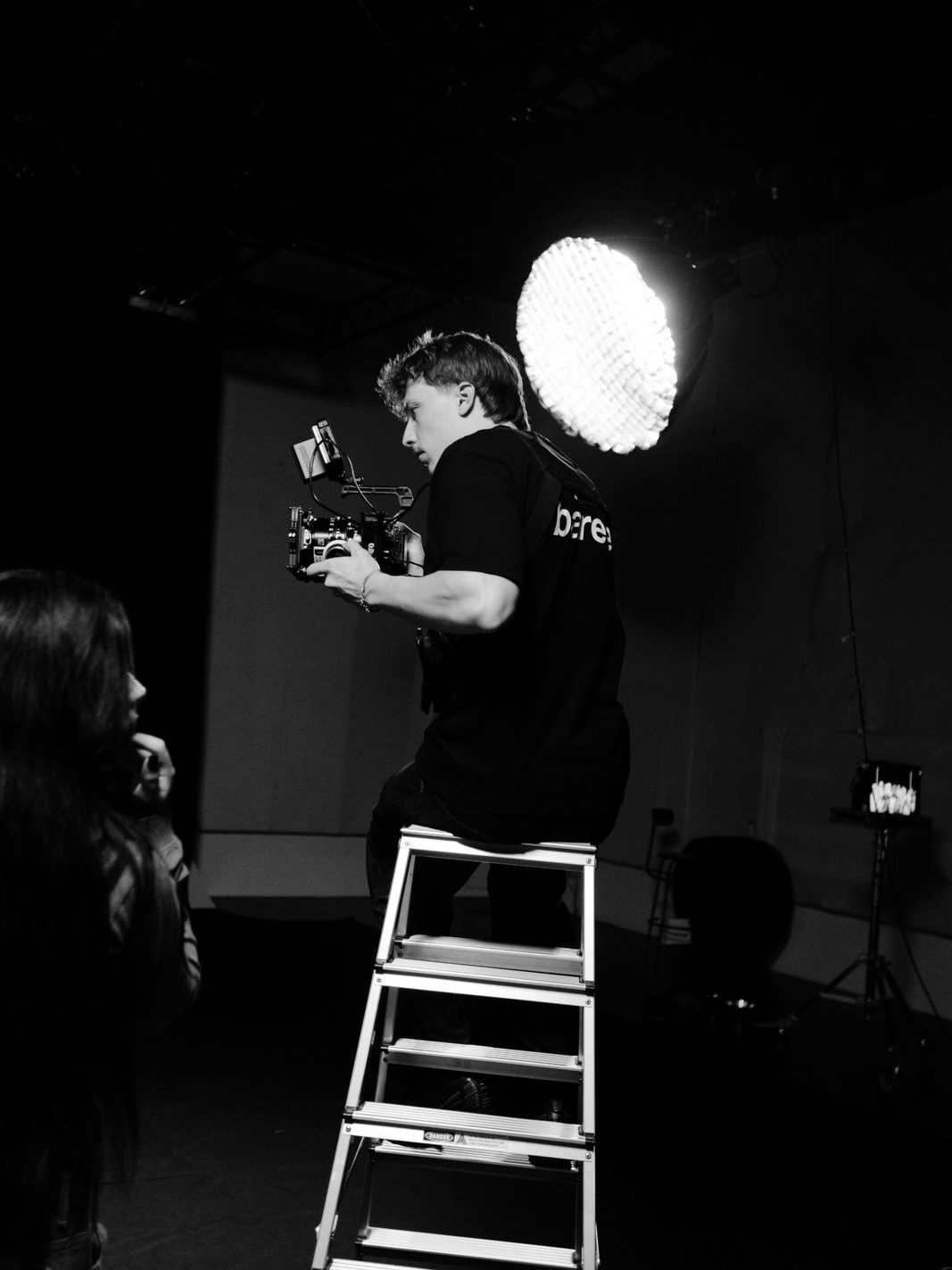 Oliver on a ladder holding a cinema camera next to a large soft light in a studio