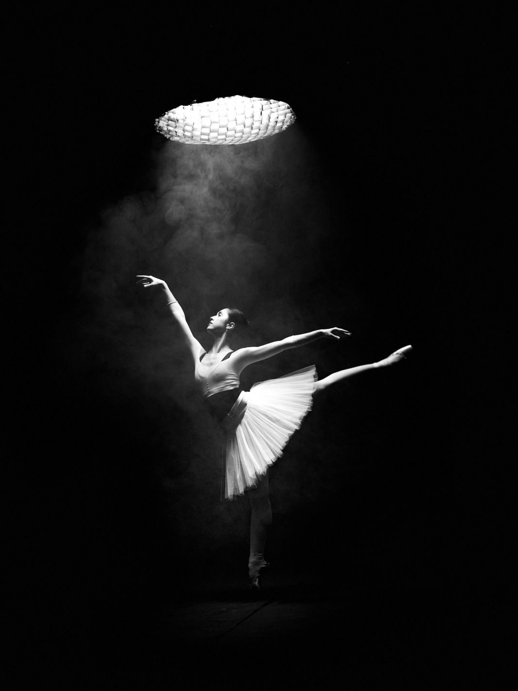 A ballet dancer in a tutu lit from above by a round soft light in haze