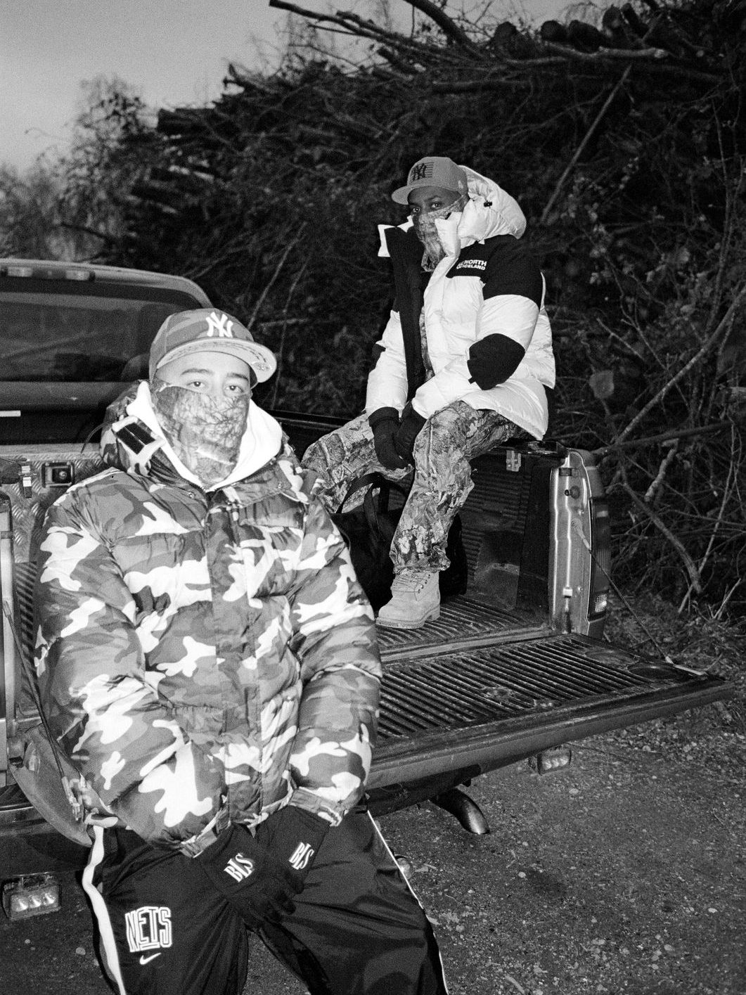 Two people in puffer jackets and face coverings on the back of a pickup truck