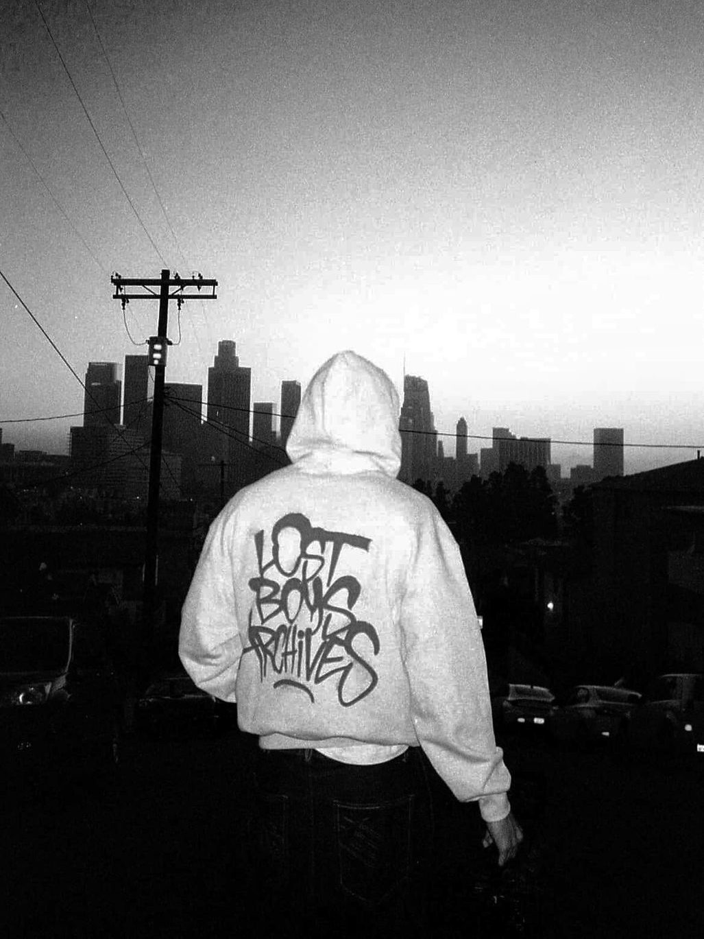 Someone in a Lost Boys Archives hoodie facing the Los Angeles skyline at dusk