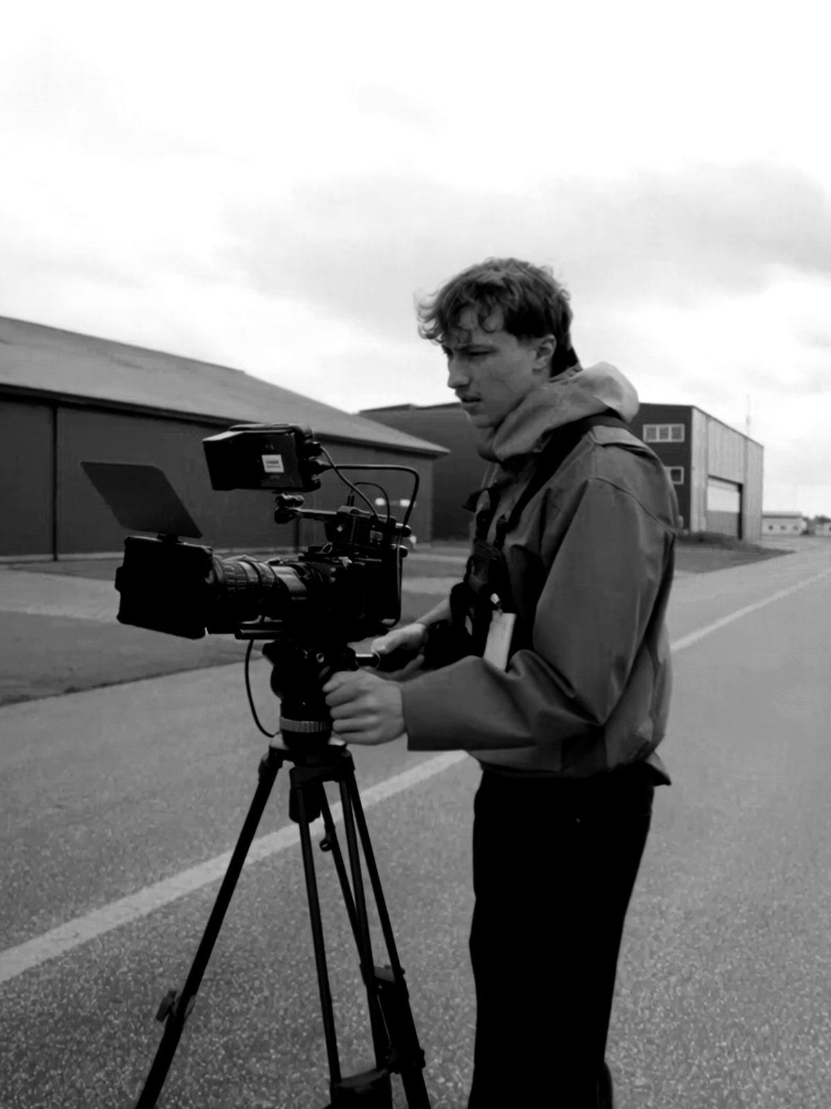 Oliver behind a cinema camera on a tripod on an airfield runway
